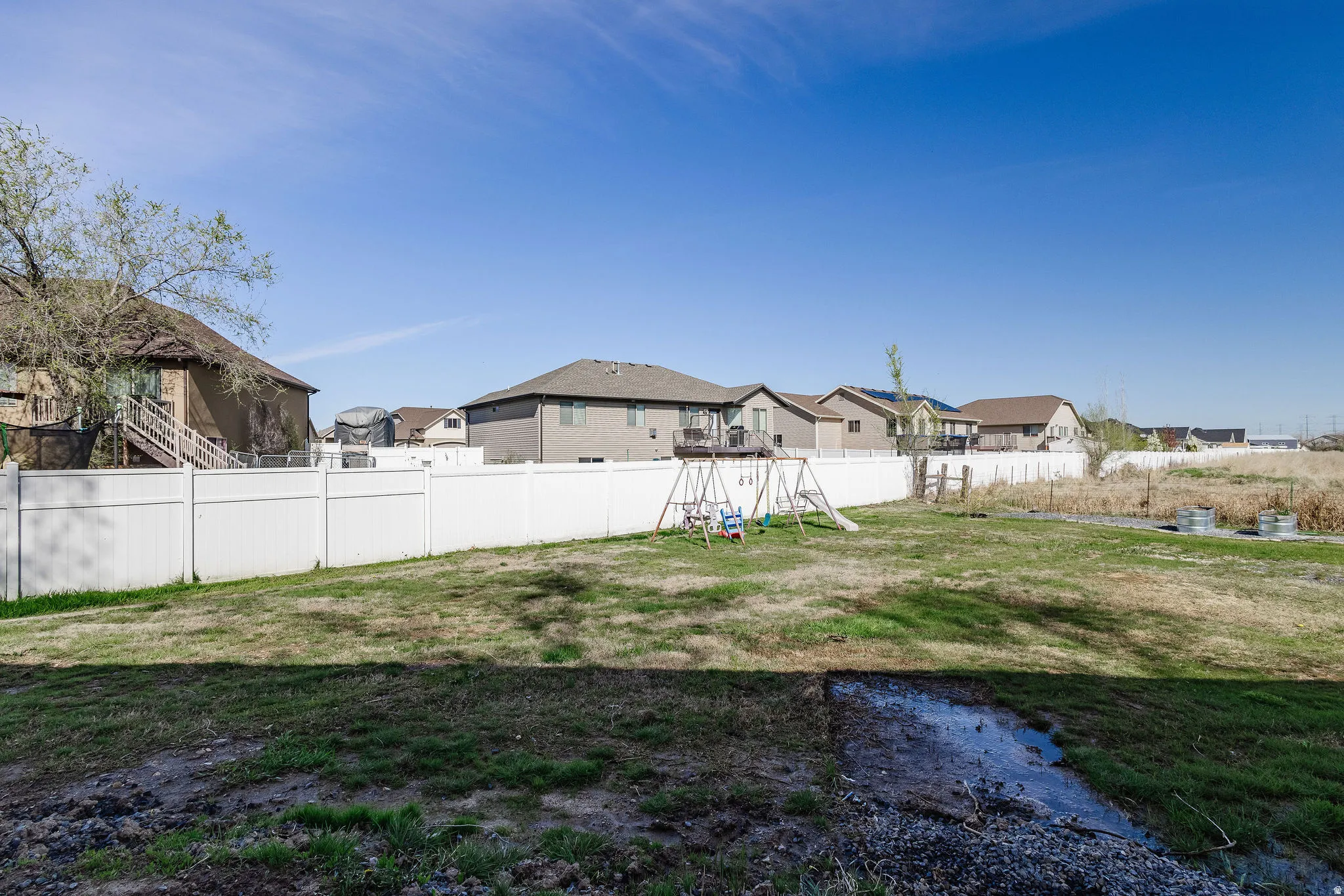 Expansive rear yard featuring green space, white privacy fencing, and distant residential structures