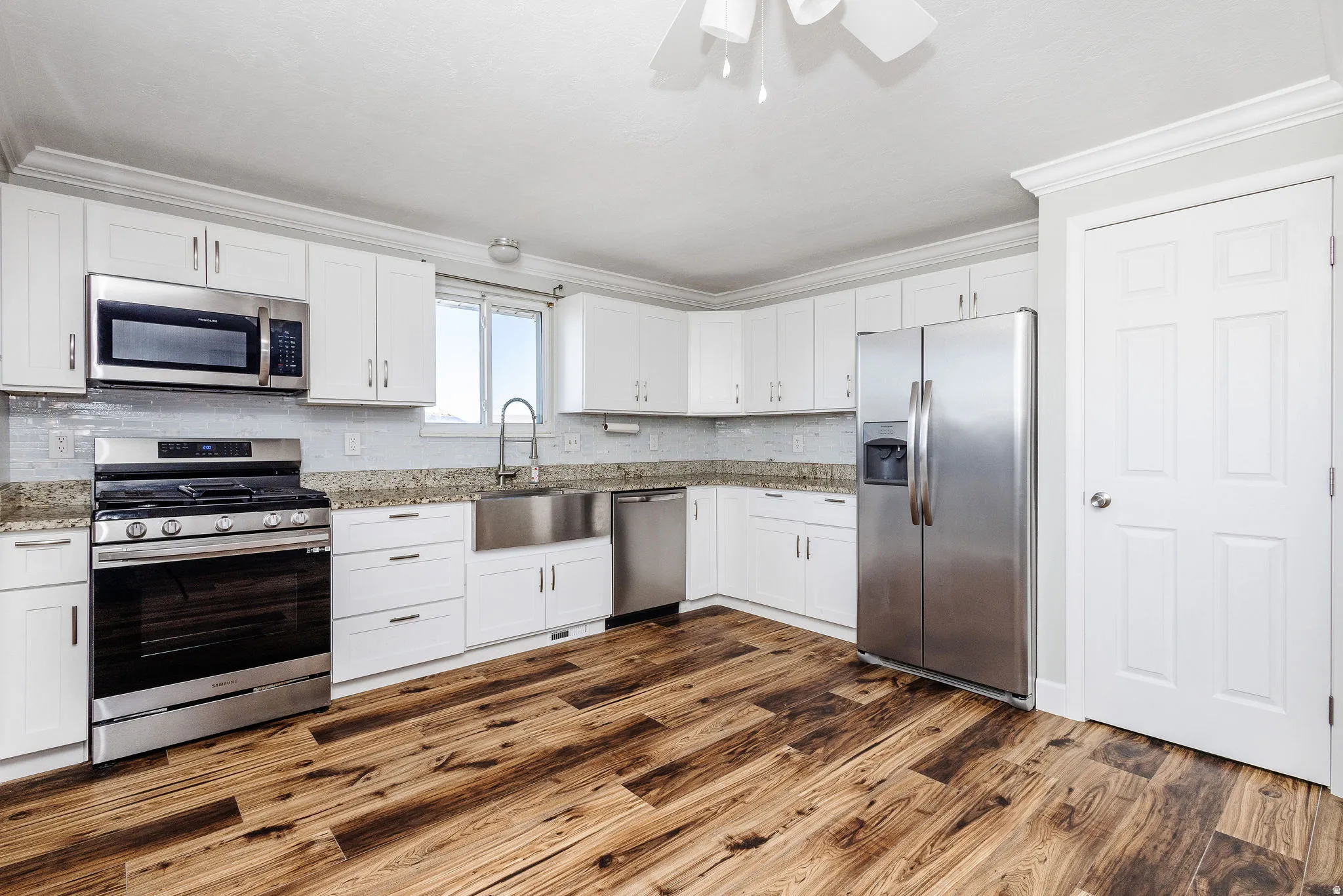 Kitchen featuring wood-finish flooring, white cabinetry, a stainless-steel appliance suite, a large farmhouse sink, and light-toned countertops