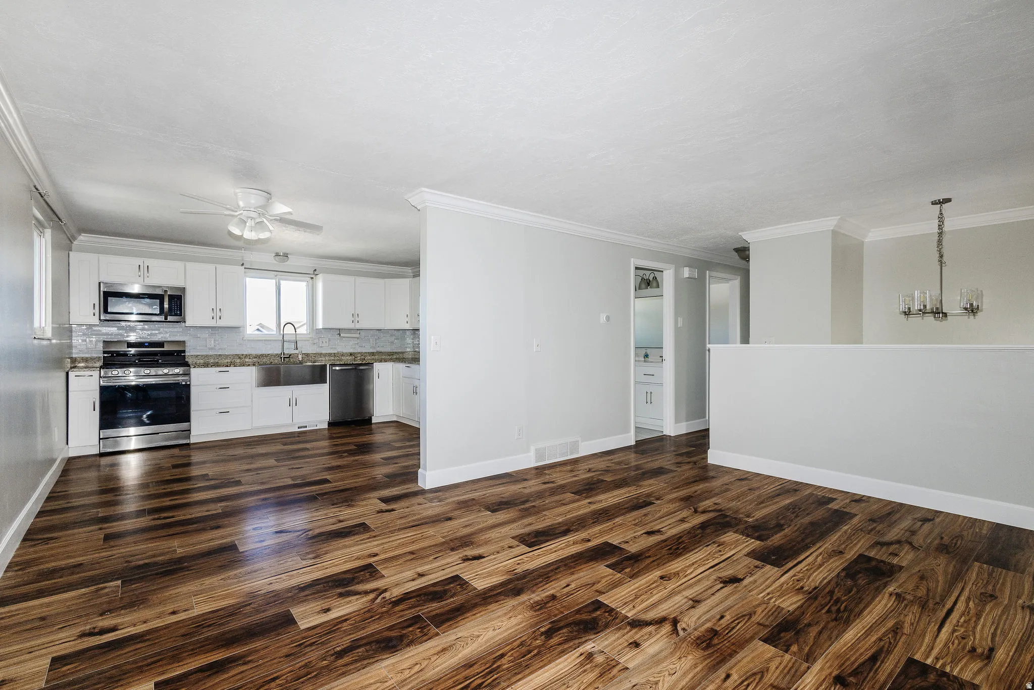 Wood-finish flooring, white cabinetry, stainless steel appliances, light-toned countertops, and a modern chandelier
