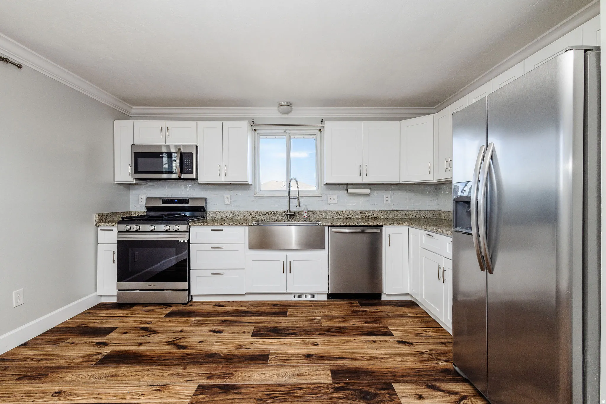 Kitchen featuring wood-finish flooring, white cabinetry, a stainless steel appliance suite, granite countertops, and a subway tile backsplash