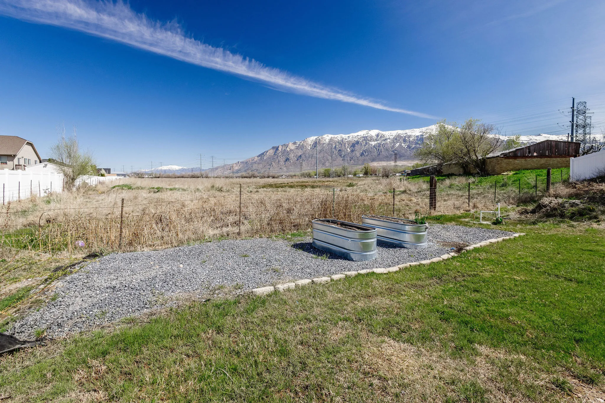 Landscaped area featuring two galvanized metal planters set on a gravel base with concrete block edging, bordered by a grassy lawn