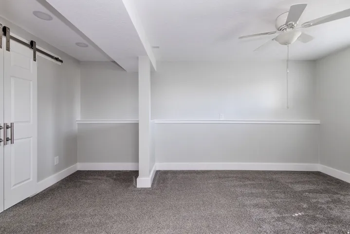 Spacious room featuring gray textured carpeting, white chair rail molding, and a ceiling fan