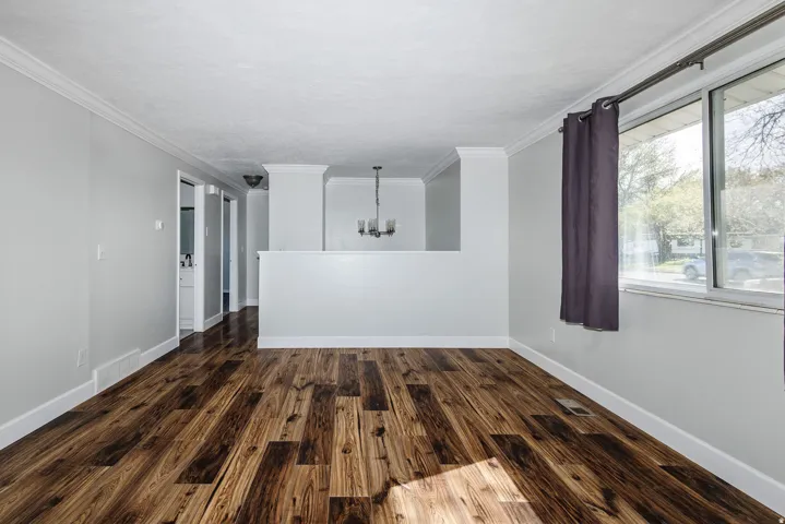 Wood-finish flooring, white crown molding, white baseboards, and a contemporary chandelier