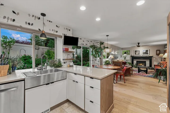 Kitchen and view of open-concept living area featuring white oak plank wood flooring, a fireplace with a black mantel, and recessed lighting