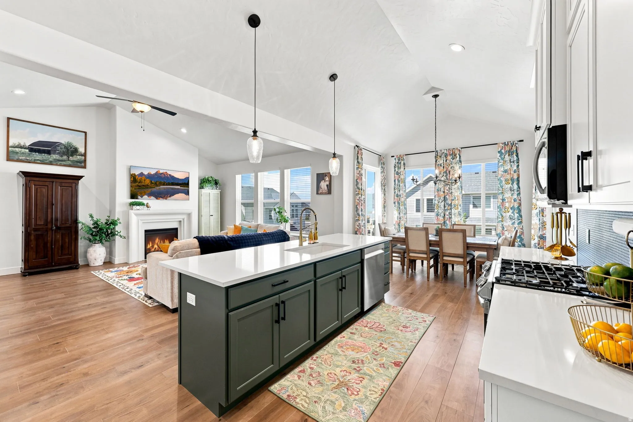 Vaulted ceilings, wood-finish flooring, a kitchen island with pendant lighting, a built-in fireplace, and expansive windows