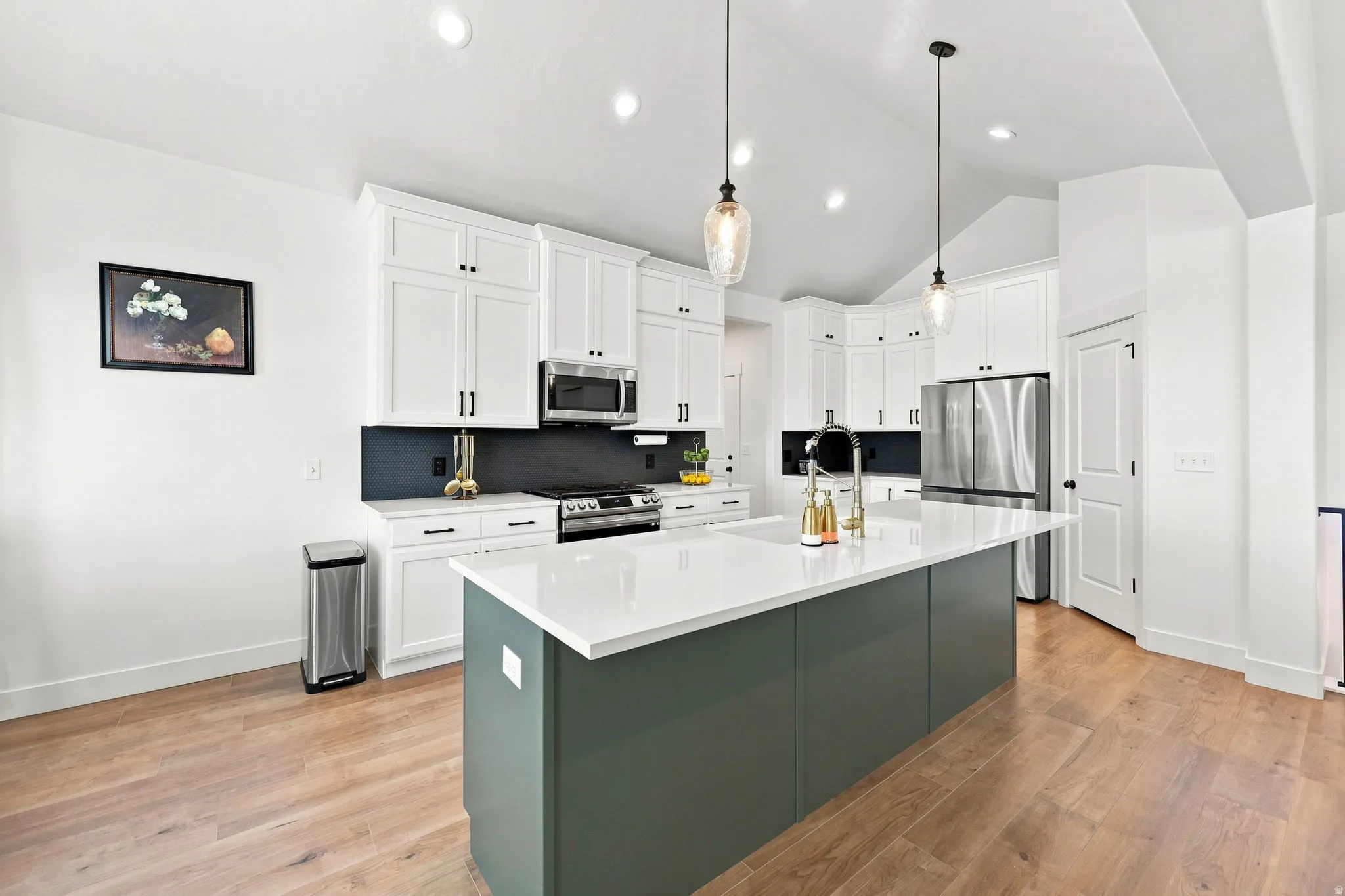 Bright kitchen featuring white cabinetry, a large center island with a white countertop, stainless steel appliances, and wood-finish flooring