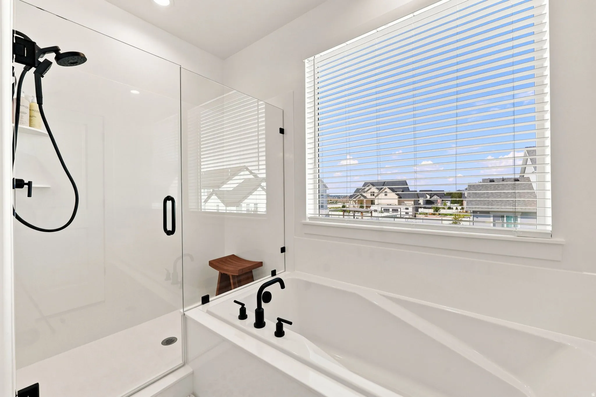 Built-in soaking tub with matte black fixtures, an adjacent walk-in shower with a glass enclosure, and a large window with horizontal blinds