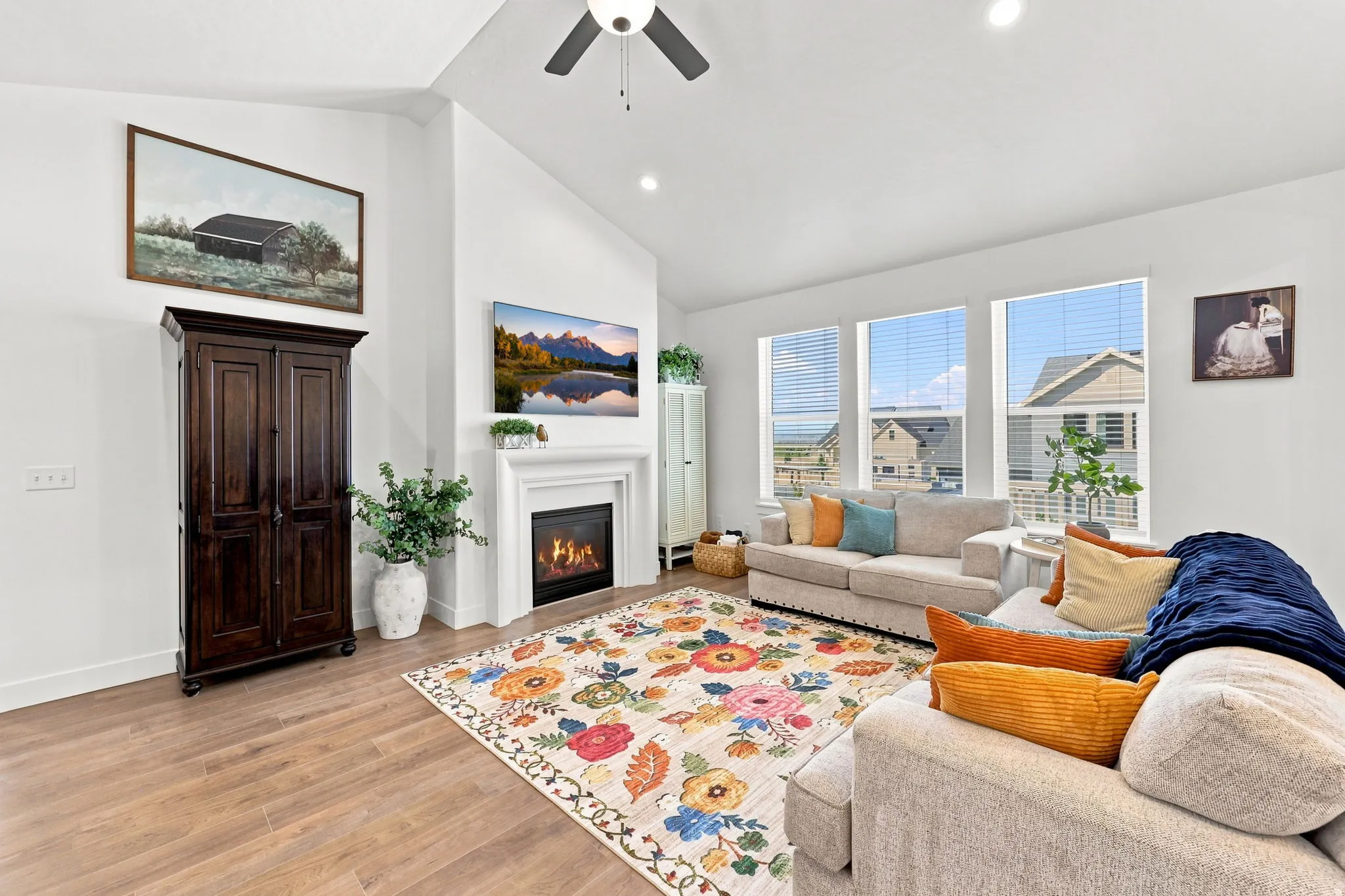 Vaulted ceiling with a ceiling fan, fireplace with a white mantel, wood-finish flooring, and multiple large windows