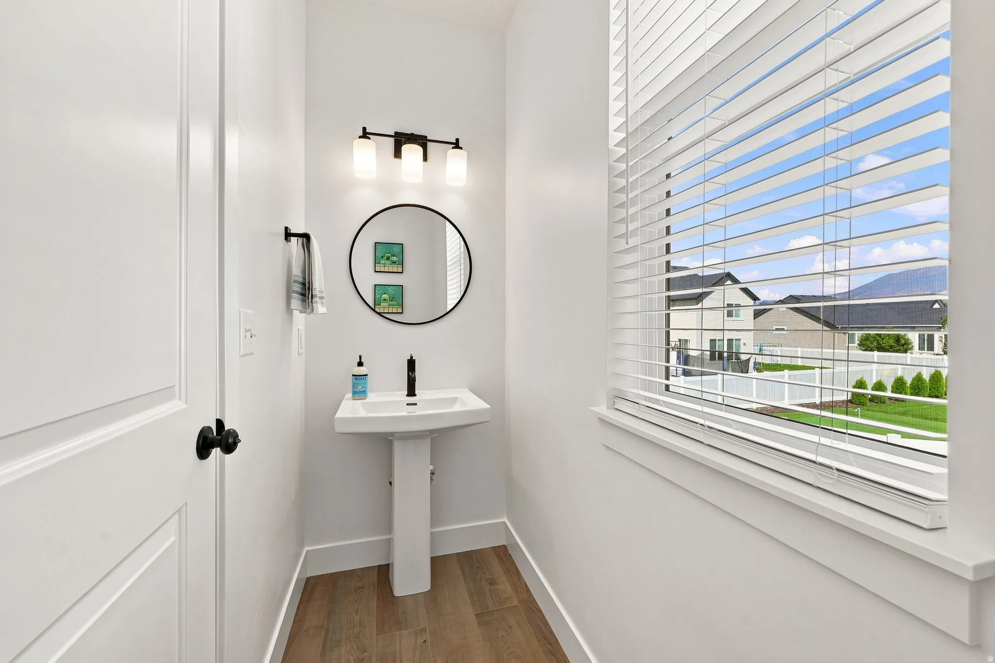 Pedestal sink with a matte black faucet, round mirror, and a three-light vanity fixture
