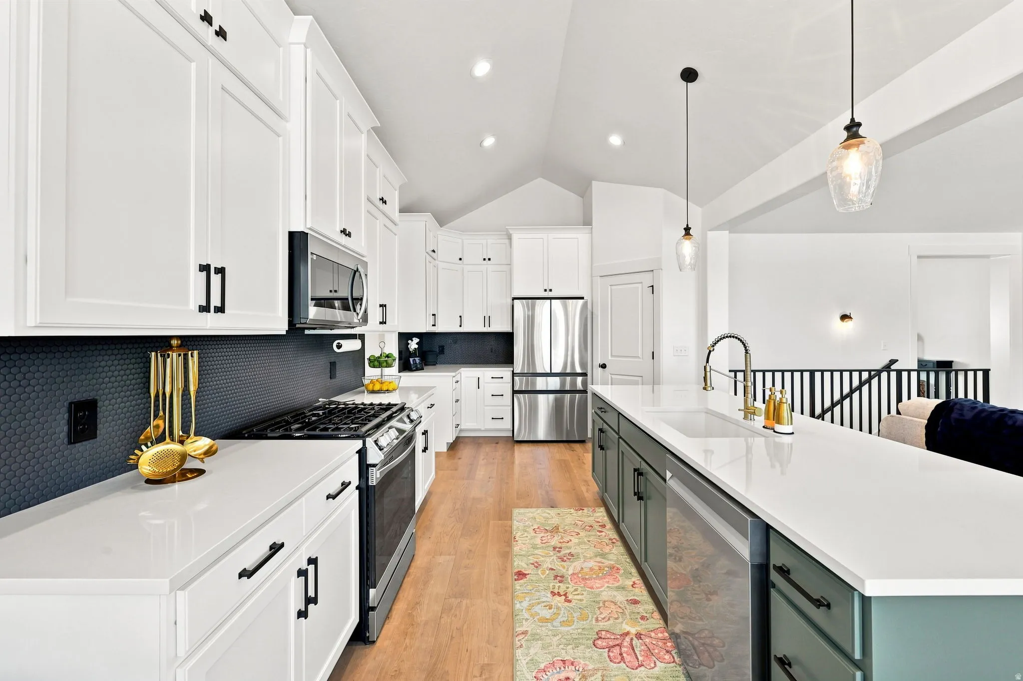 White cabinetry with black hardware, dark hexagonal tile backsplash, stainless steel appliances, light wood-finish flooring, and a vaulted ceiling