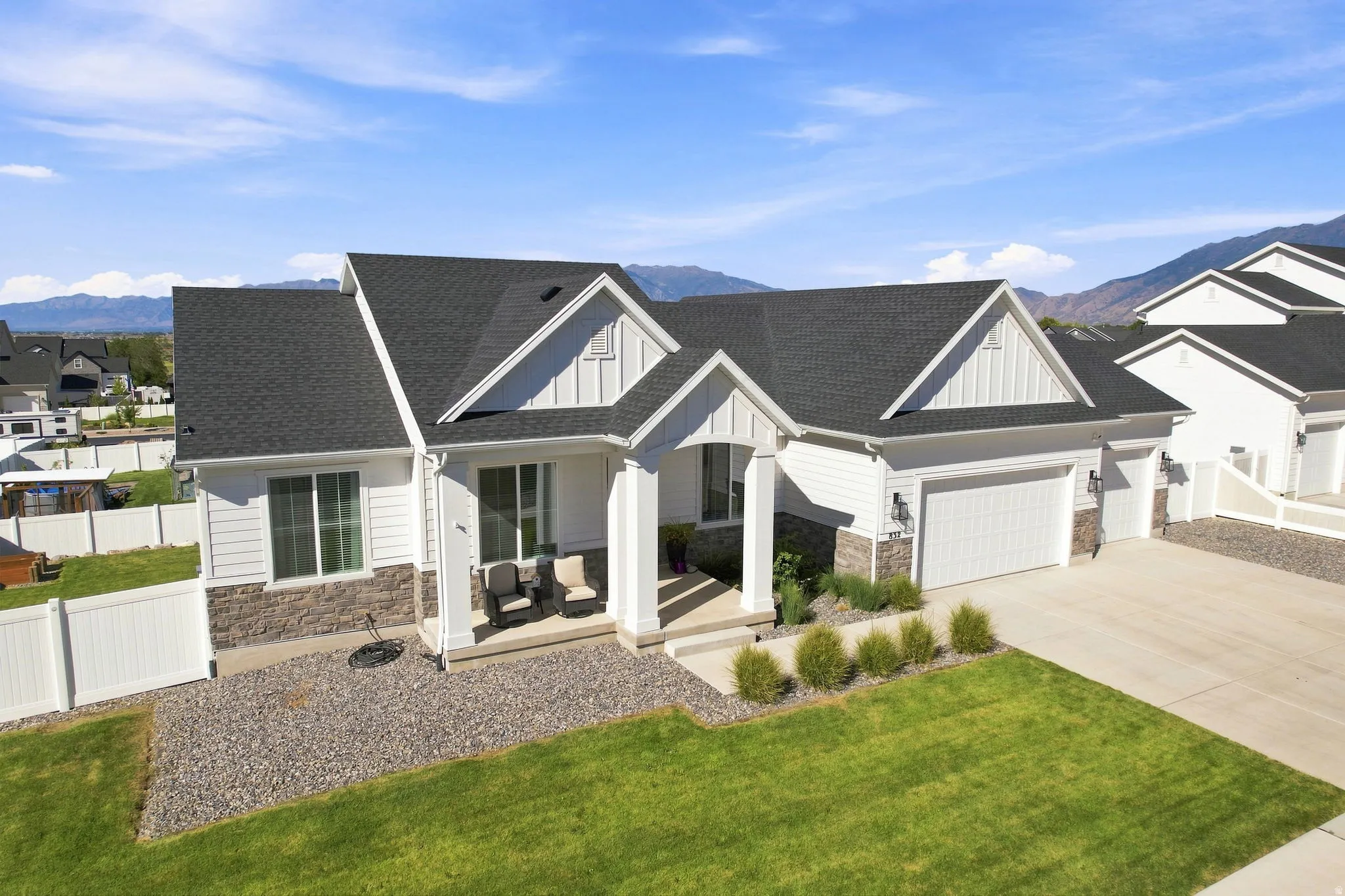 White siding exterior with a dark shingle roof, stone veneer accents, an attached garage, and a concrete driveway