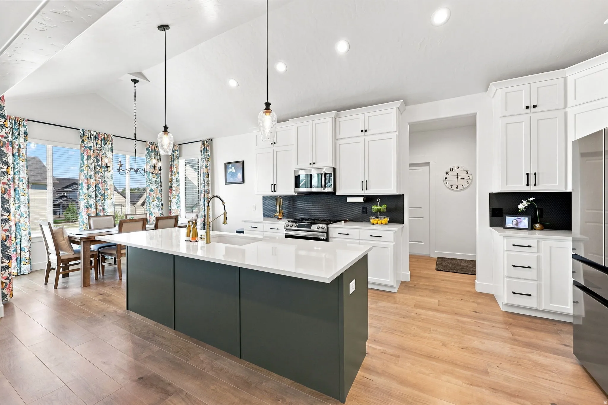 Vaulted ceilings, wood-finish flooring, white cabinetry, dark gray kitchen island, and a stainless steel refrigerator