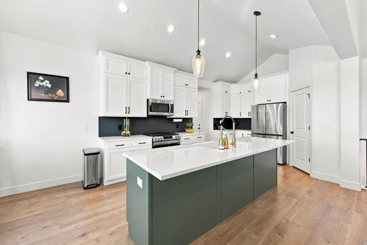 Bright kitchen featuring white cabinetry, a large center island with a white countertop, stainless steel appliances, and wood-finish flooring