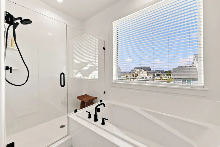 Built-in soaking tub with matte black fixtures, an adjacent walk-in shower with a glass enclosure, and a large window with horizontal blinds