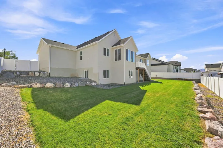Expansive grassy lawn with a gravel border, featuring a stucco exterior with multiple windows, and a raised exterior deck with stairs