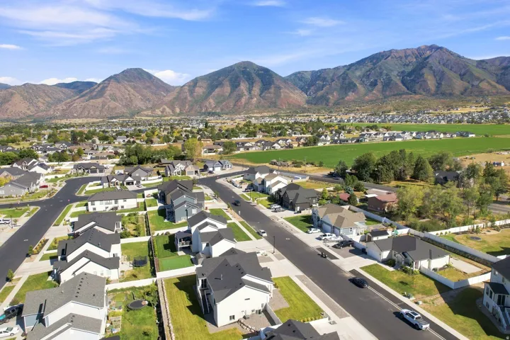 Aerial perspective showcasing a residential community with paved streets, surrounded by expansive green fields and distant mountains