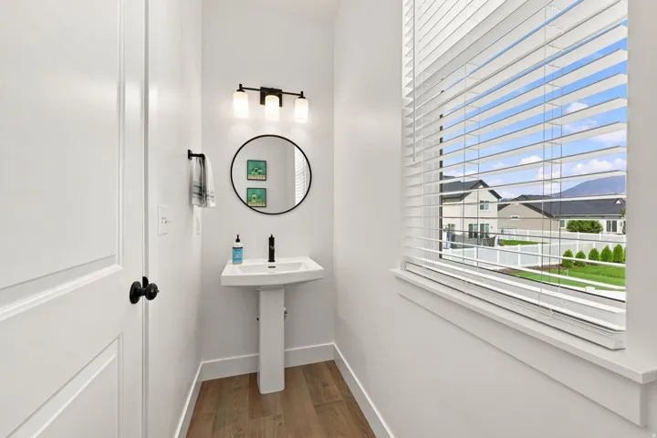 Pedestal sink with a matte black faucet, round mirror, and a three-light vanity fixture