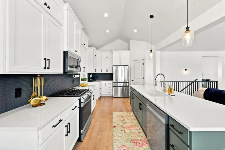 White cabinetry with black hardware, dark hexagonal tile backsplash, stainless steel appliances, light wood-finish flooring, and a vaulted ceiling