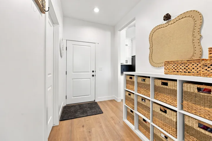 Hardwood-style flooring, white paneled door, built-in shelving, recessed lighting, and crisp white walls