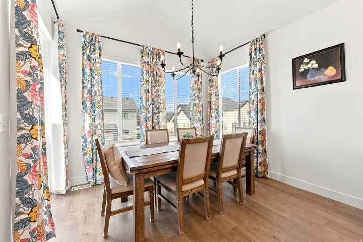 Vaulted ceiling with an elegant chandelier, expansive windows with horizontal blinds, and wood-finish flooring