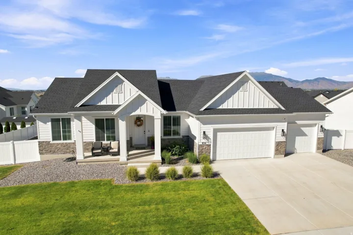 White exterior with stone accents, covered front porch, attached multi-car garage, and a manicured lawn