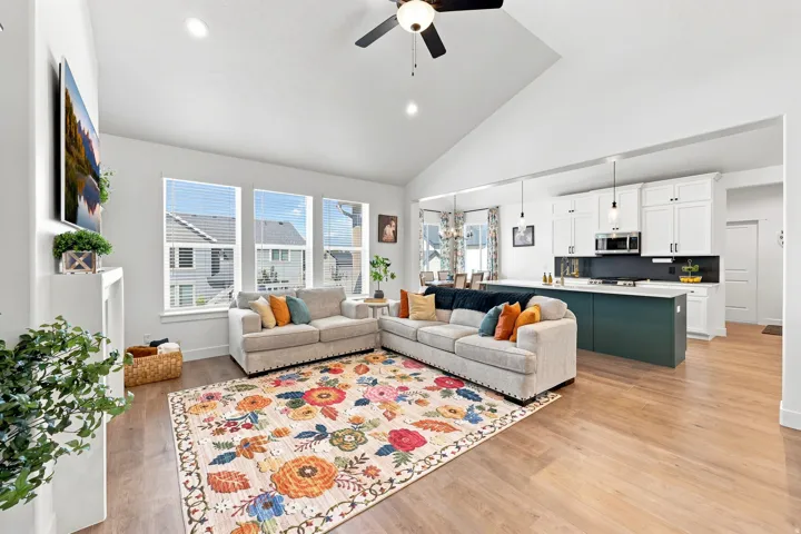 Open-concept living space with vaulted ceilings, wood-finish flooring, a white fireplace, and a kitchen featuring white cabinetry and a contrasting island