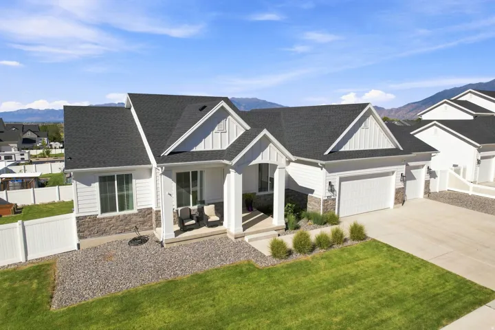 White siding exterior with a dark shingle roof, stone veneer accents, an attached garage, and a concrete driveway