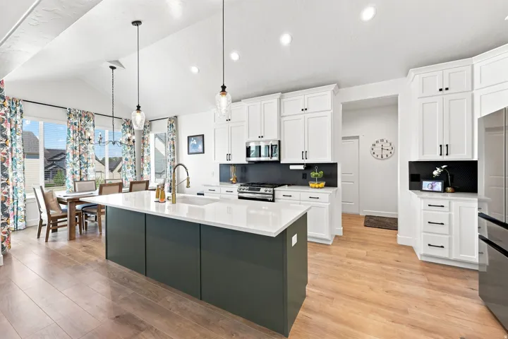 Vaulted ceilings, wood-finish flooring, white cabinetry, dark gray kitchen island, and a stainless steel refrigerator