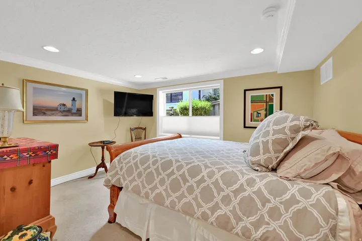 Recessed ceiling lighting, crown molding, a window with cellular blinds, and wall-mounted television are featured