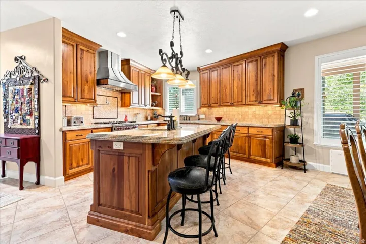 Kitchen featuring wood cabinetry, a center island with countertop seating, tiled flooring, a stainless steel range hood, and a tiled backsplash