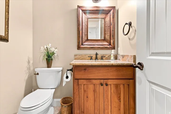 Wood-finish vanity with a stone countertop, bronze faucet, and a framed mirror