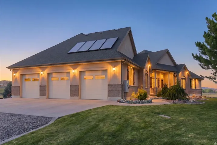 Stucco and brick exterior with a three-car garage, solar panels, a covered entry, and landscaped rock accents
