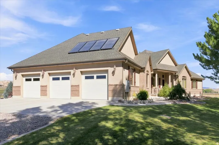 Stucco and brick exterior with a three-car garage, solar panels, a covered entry, and a manicured lawn