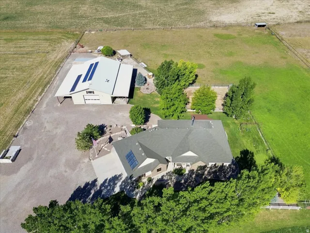 Expansive property featuring a large outbuilding with solar panels, a residence with a dark roof and solar panels, and mature trees