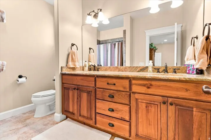 Dual vanity with wood cabinetry, integrated sinks, bronze-finish fixtures, and a large wall-mounted mirror