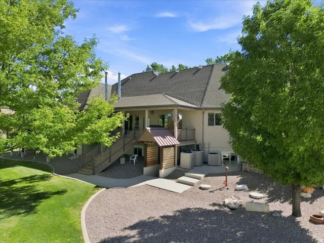 Expansive backyard featuring a covered patio, tiered deck with railings, concrete pathways, and a gravel-covered area