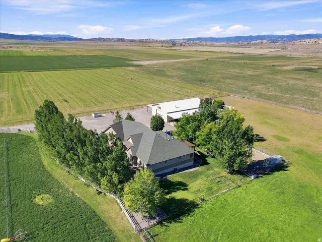 Countryside estate nestled on expansive grounds featuring a two-story residence with a charcoal-toned roof, mature landscaping with established trees providing natural screening, a large agricultural outbuilding, and manicured lawn acreage with distant mo