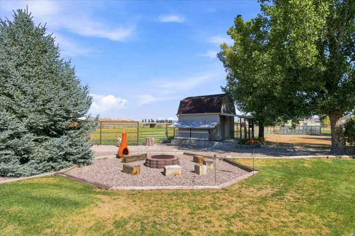 Expansive backyard featuring a gravel fire pit area, manicured lawn, mature trees, and a barn structure
