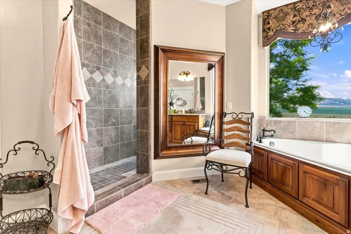 Walk-in shower with tiled surround, soaking tub with wood-paneled base, and a large window