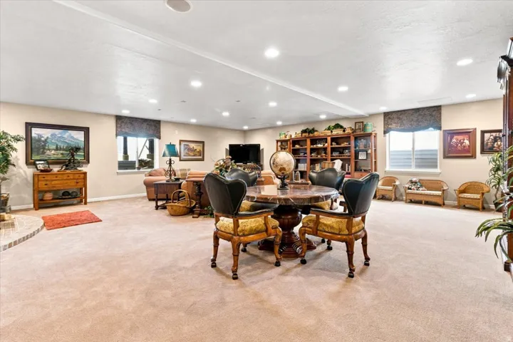 Recessed lighting illuminates this expansive space featuring neutral carpeting, a built-in wooden bookcase, and natural light from multiple windows
