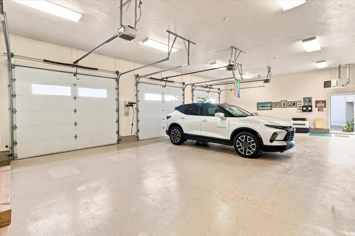Multi-vehicle garage with three overhead doors featuring window panels, a durable epoxy-coated concrete floor, and overhead fluorescent lighting