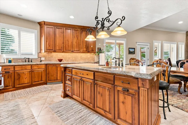Kitchen featuring extensive wood cabinetry, a central island with a built-in sink, stone countertops, and tile flooring