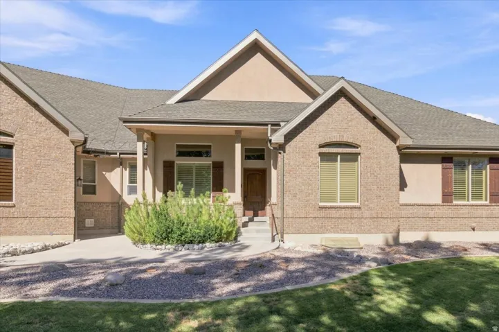 Brick and stucco exterior, covered entry porch, wood-finish shutters, arched window, and a gray shingle roof