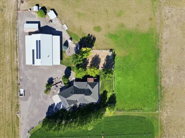 Expansive property featuring a primary residence with a dark shingle roof, a large ancillary building with solar panels, and extensive surrounding green space