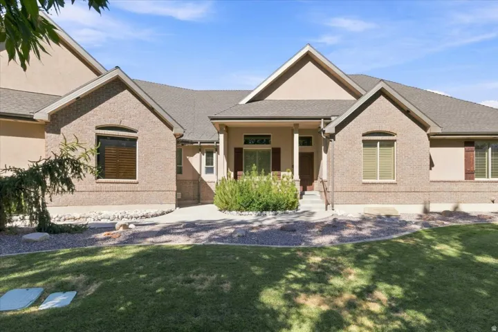 Brick and stucco exterior, covered front porch, gabled rooflines, mature landscaping, and an expansive lawn
