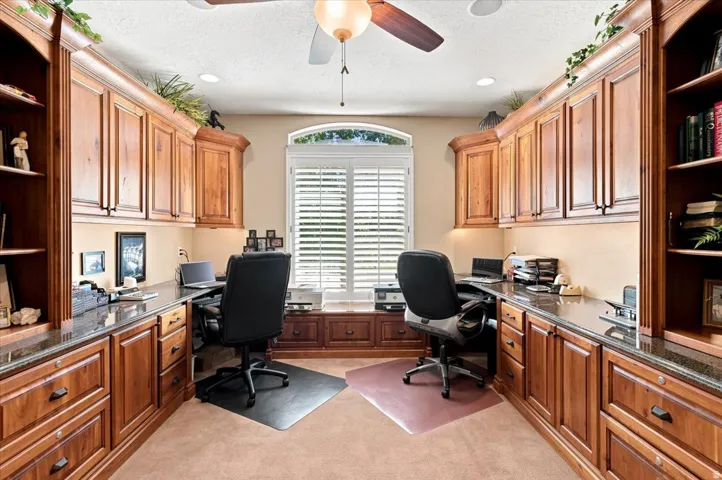 Built-in wood cabinetry with a dark stone countertop, an arched window with plantation shutters, and a ceiling fan with integrated lighting