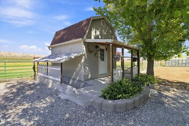 Gabled roof structure with a covered porch, white picket fence, concrete patio, and a decorative concrete block planter