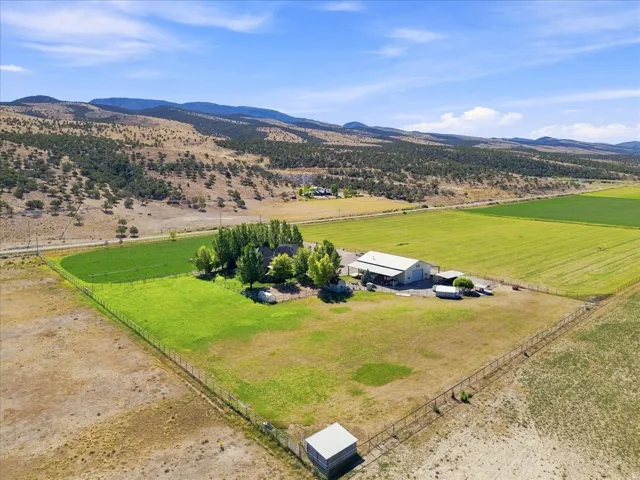 Expansive rural property featuring a large structure with a metal roof, surrounded by mature trees and fenced pasture land