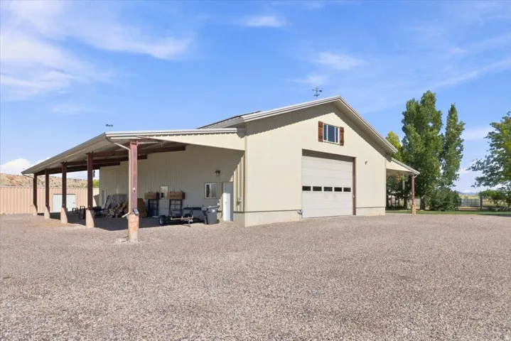 Detached structure featuring a neutral-toned metal exterior, an extended covered awning, a large roll-up garage door, and an upper-level window with decorative shutters