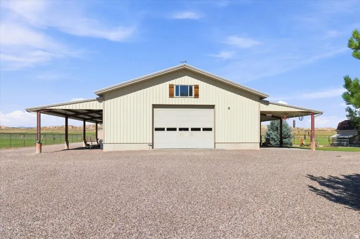Metal-sided structure featuring a large garage door, dual side awnings, and a gravel foreground